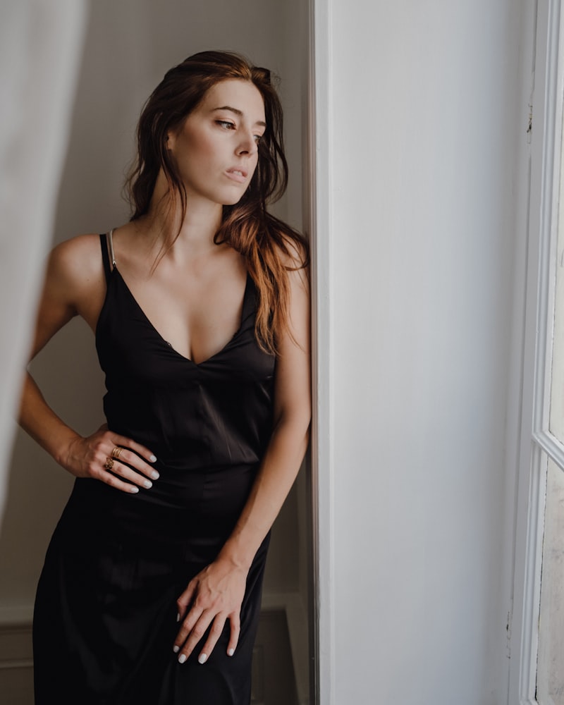 A woman in a black washed-silk slip by a window