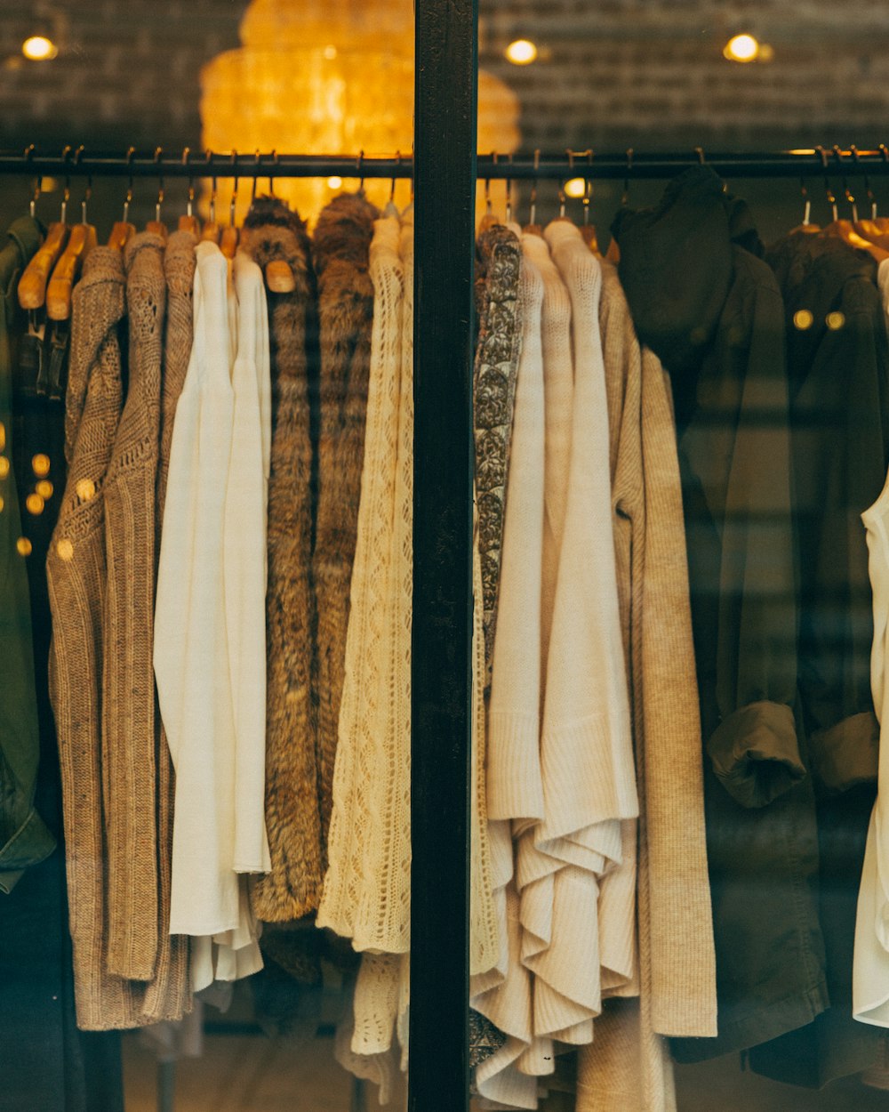 A warm-lit window of vintage knitwear on wooden hangers