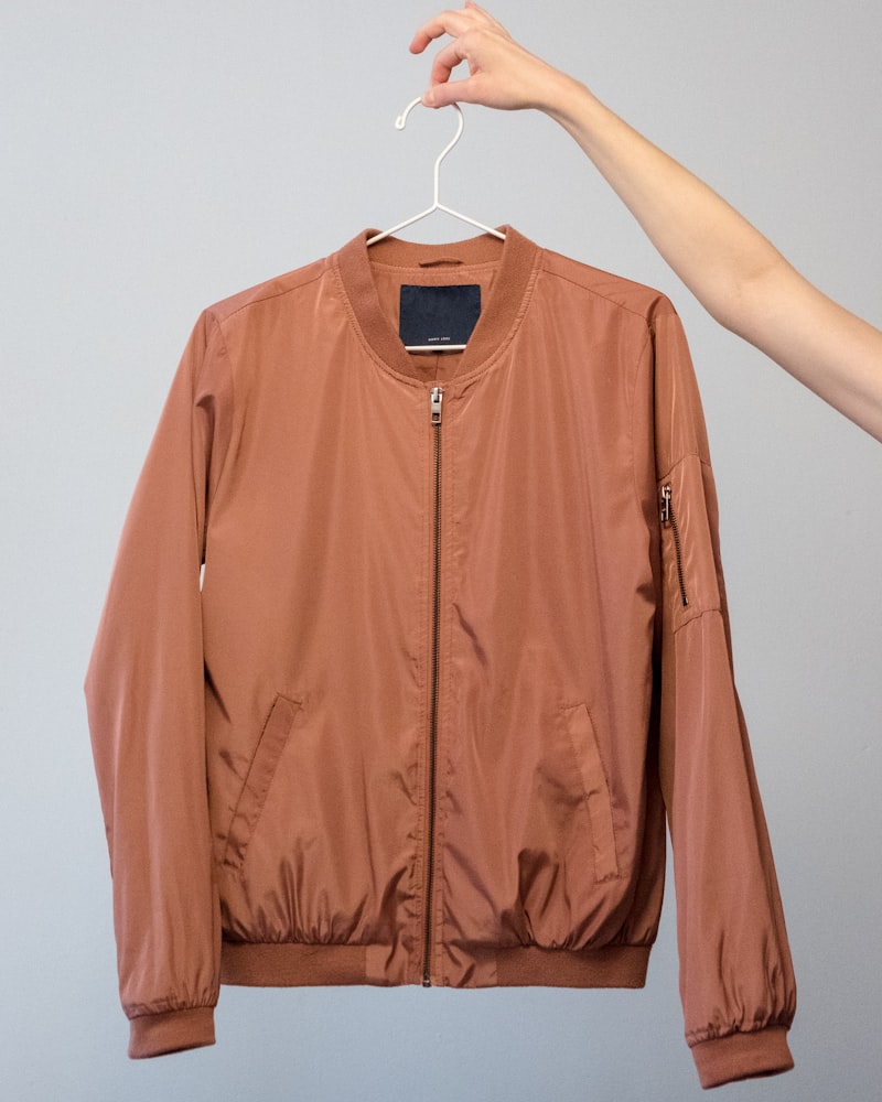 A terracotta nylon bomber jacket on a hanger