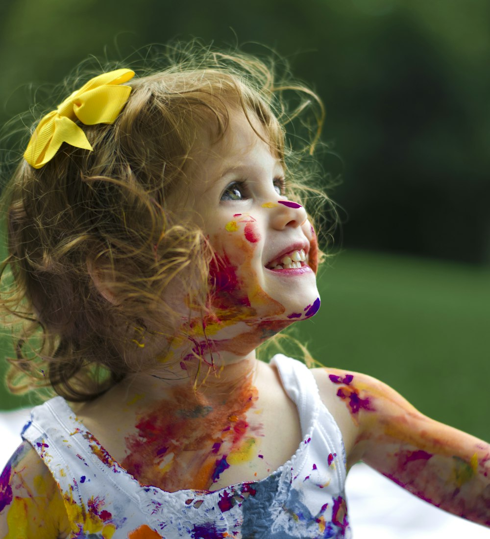 A joyful toddler covered head to toe in colourful paint, mid-laugh
