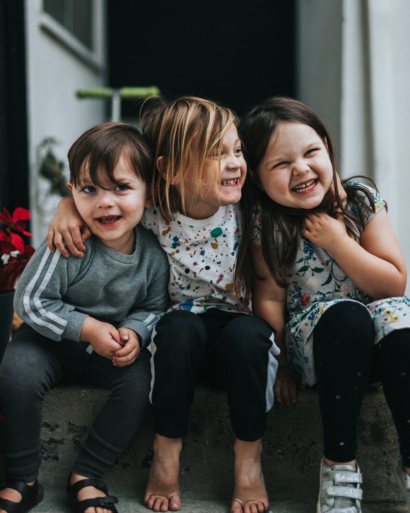 Three little kids laughing together on a doorstep
