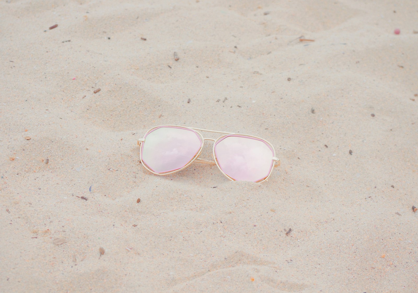 A pair of black Aether sunglasses resting in golden sand by the sea