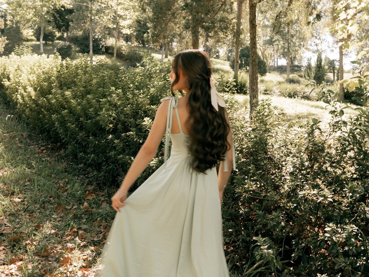 A person walking through a sunlit garden in soft, natural clothing