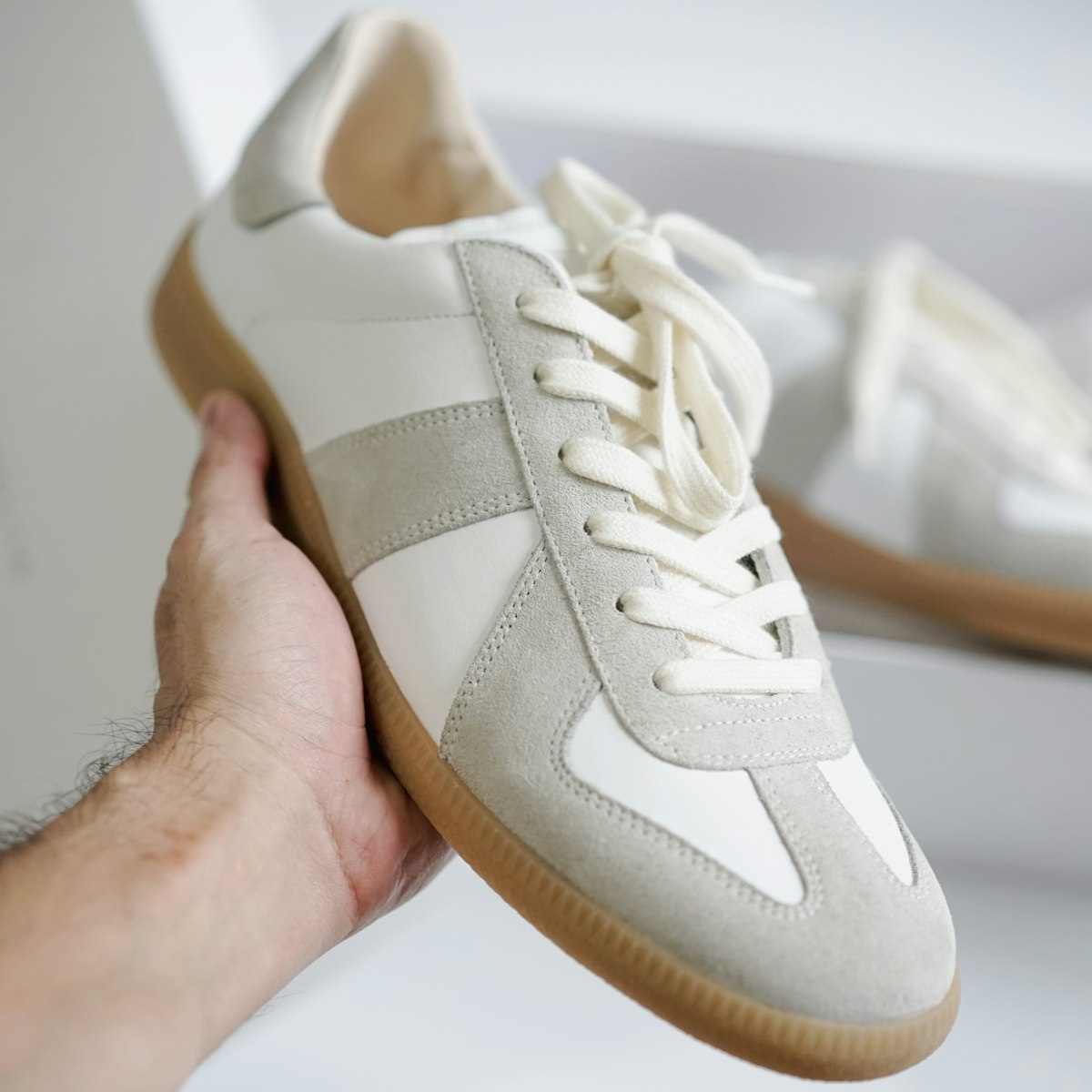 The Everyday Sneaker in Oat, a knit eco sneaker held in hand against a soft daylight backdrop