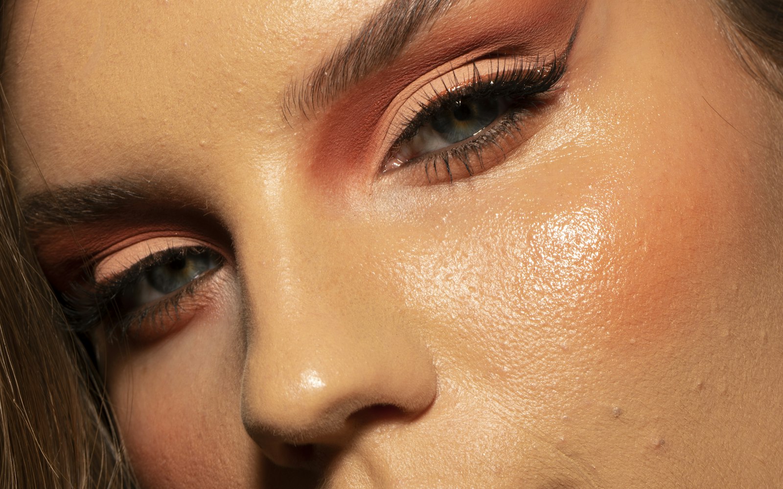 A glowing close-up of warm coral and copper eye makeup on radiant skin