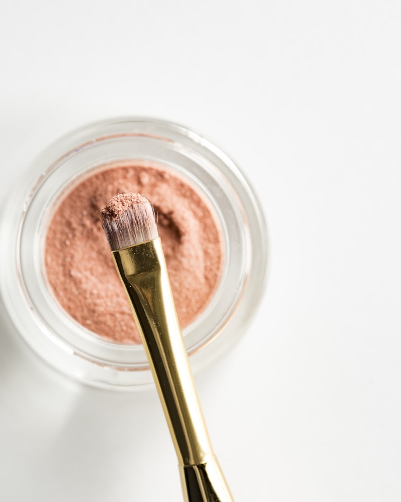 An eyeshadow pot with a gold-handled brush and rose powder