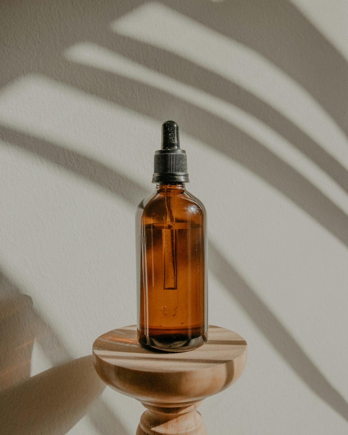 An amber glass skincare bottle on a wooden stand in soft daylight