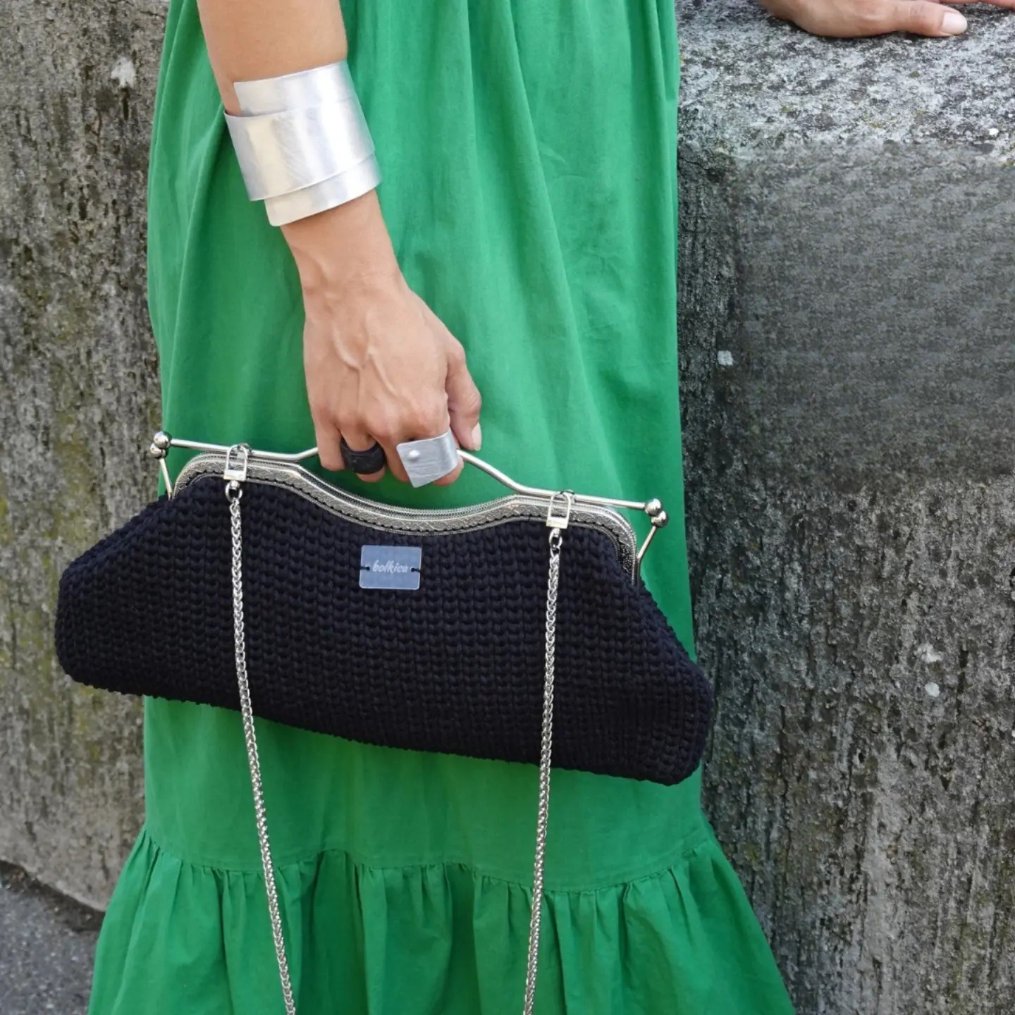 A black crochet clutch held against a green dress