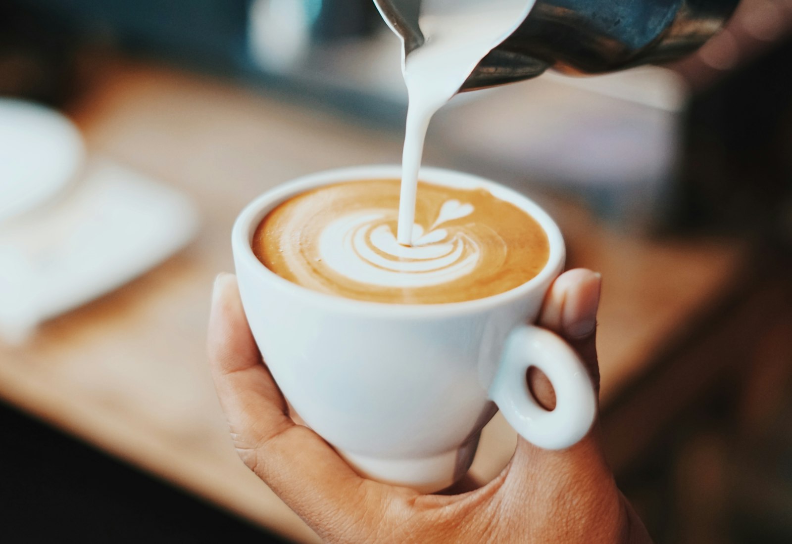 A barista pouring latte art into a ceramic cup at the Kindred Coffee bar