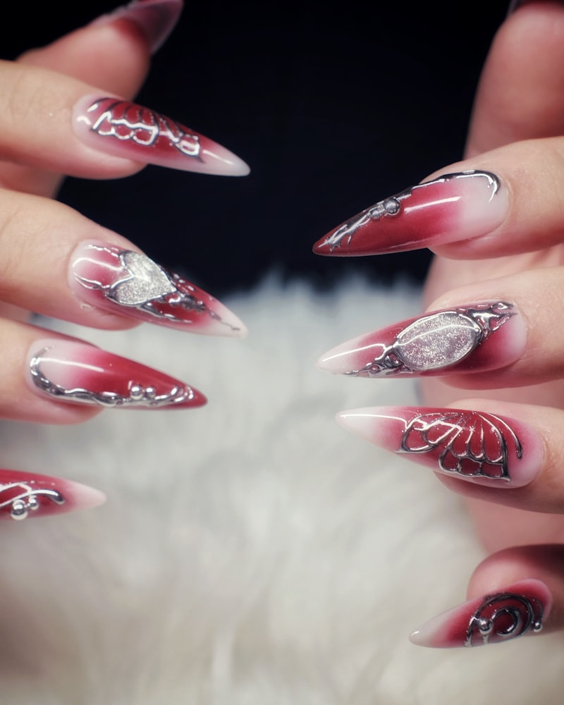 Statement deep-red stiletto nails with silver chrome charms and crystal accents