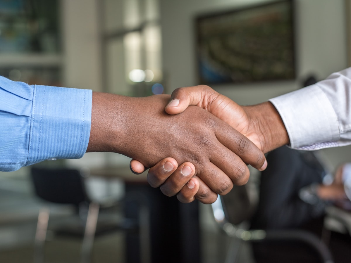 Two people shaking hands across a desk in a bright office