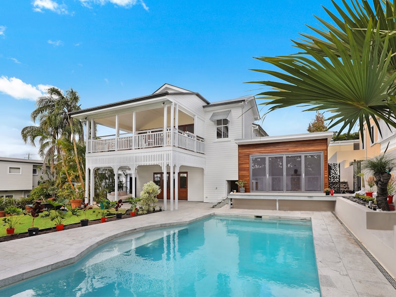 White weatherboard two-storey home with a poolside terrace and timber accents