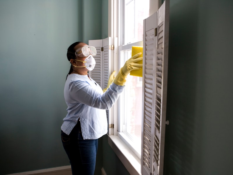 Cleaner in protective gear wiping a window with a yellow sponge
