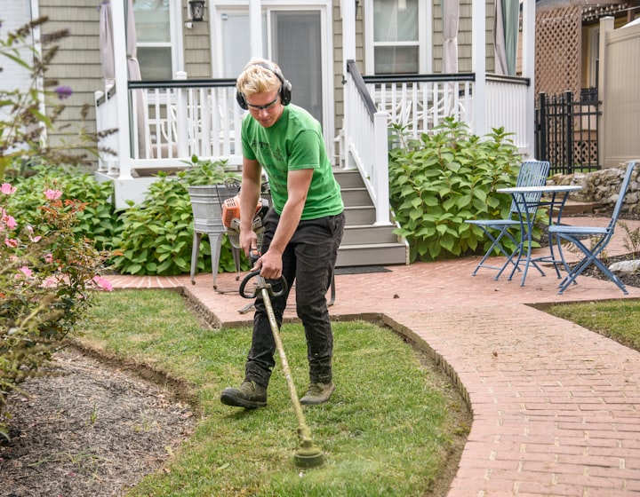 A landscaper edging a manicured lawn beside a brick garden path
