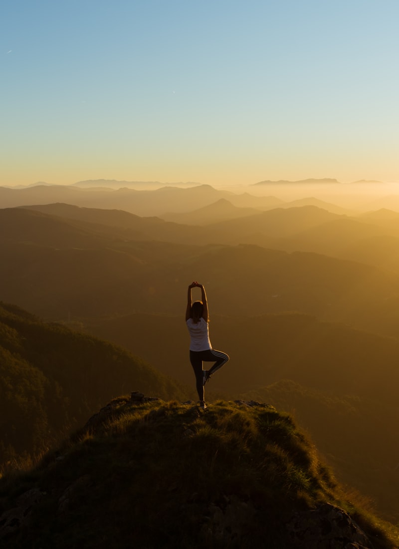 Silhouette of a person stretching on a mountaintop at golden sunrise