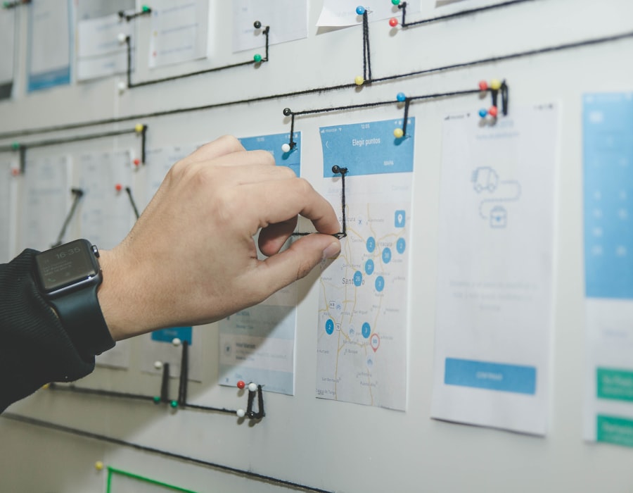 Hand mapping a user-onboarding flow with mobile mockups pinned to a wall