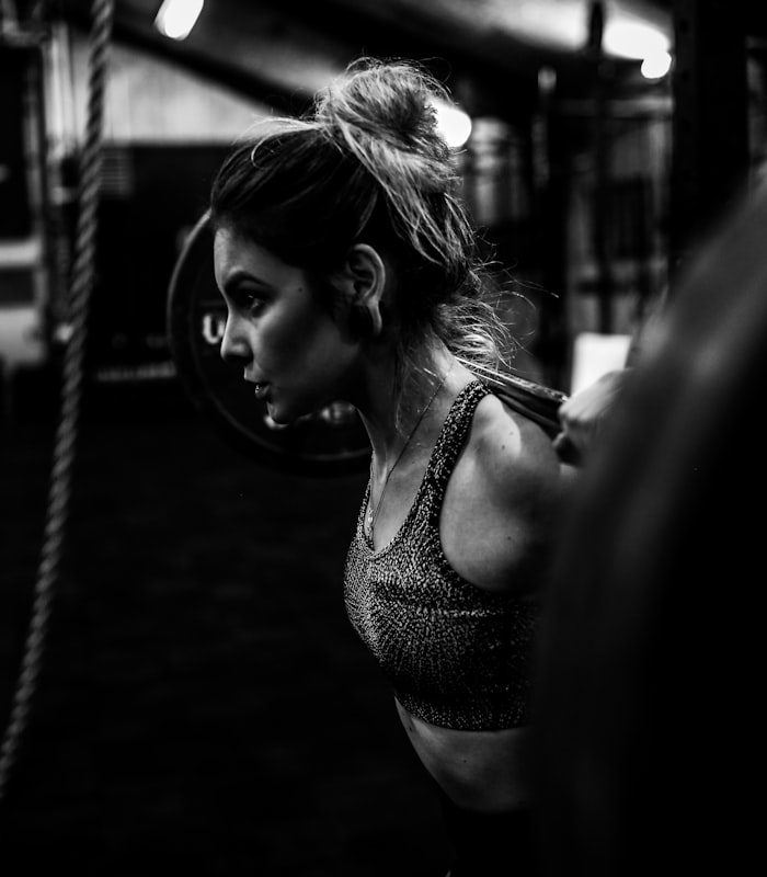 Client Sofia squatting under a loaded barbell in low light