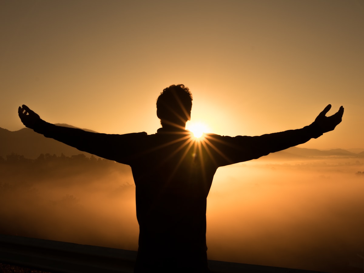 Silhouette of a person standing with arms open against a glowing sunrise sky
