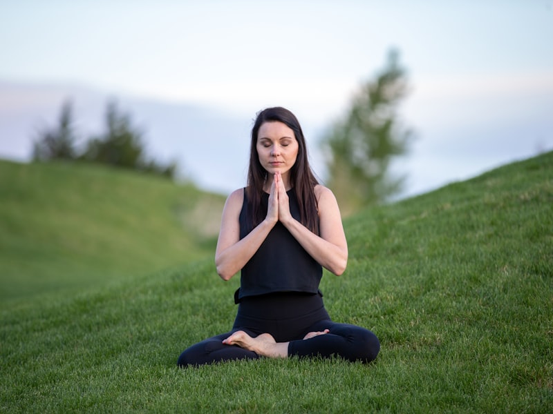 A woman sitting cross-legged in a calm meditation pose on a grassy hillside at dusk