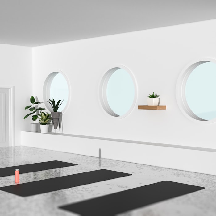 A bright, minimal yoga studio with round windows, plants and dark mats on the floor
