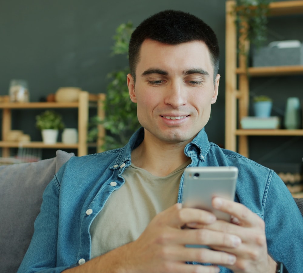 Relaxed man smiling at his phone on a couch at home
