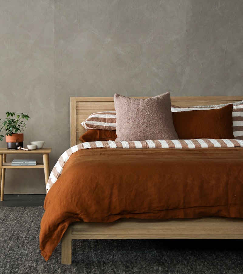 A bed dressed in warm terracotta linen with striped and boucle cushions