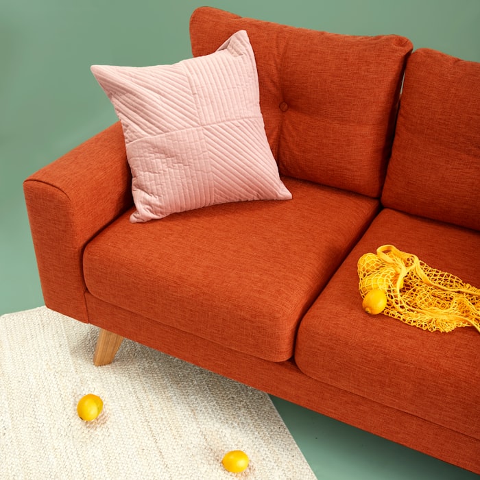 A terracotta sofa styled with a soft blush quilted cushion and a woven rug