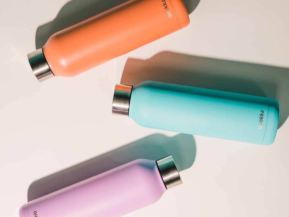 Three Hale bottles in burnt clay, teal, and lilac arranged on a soft cream surface