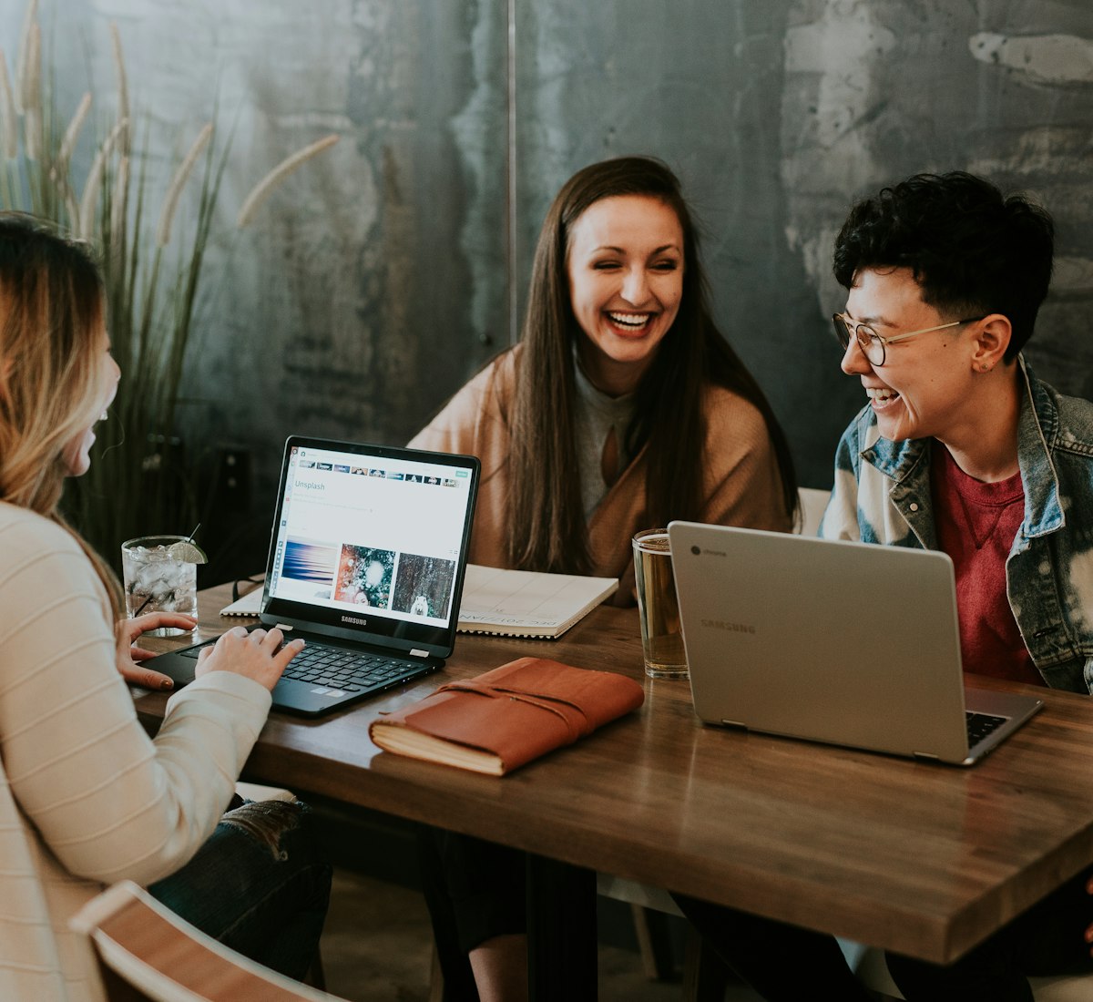 Three students smiling and learning together on laptops at a shared desk