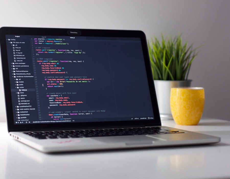 A laptop on a clean desk showing JavaScript code in an editor beside a small plant
