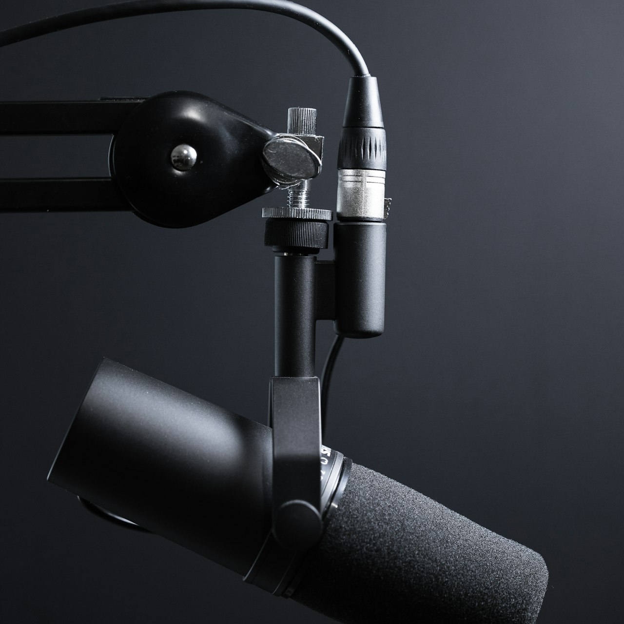 Studio broadcast microphone on a boom arm against a dark backdrop