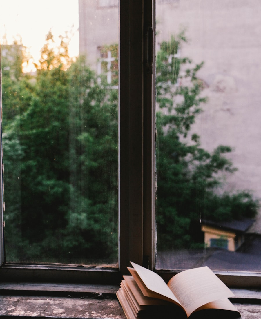 An open book resting on a windowsill at dusk, golden light spilling through the trees outside
