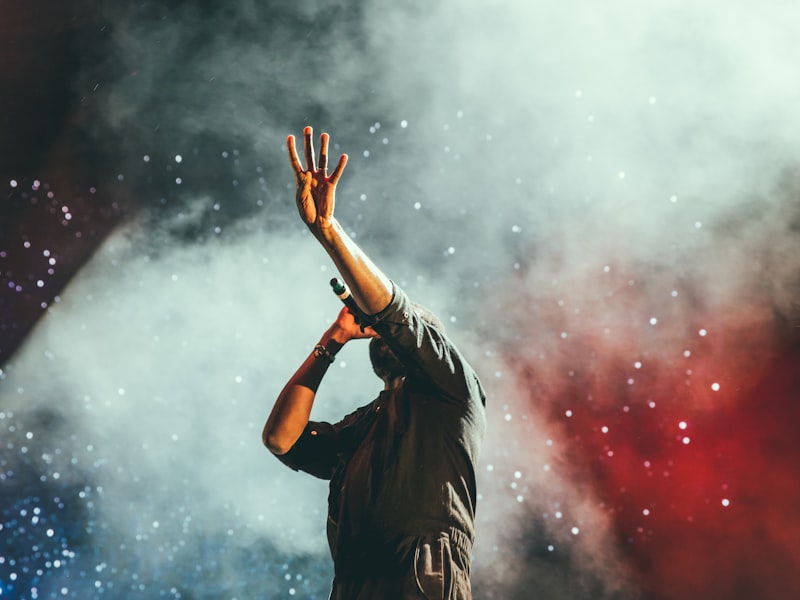 Singer with a raised hand silhouetted against red and blue stage smoke