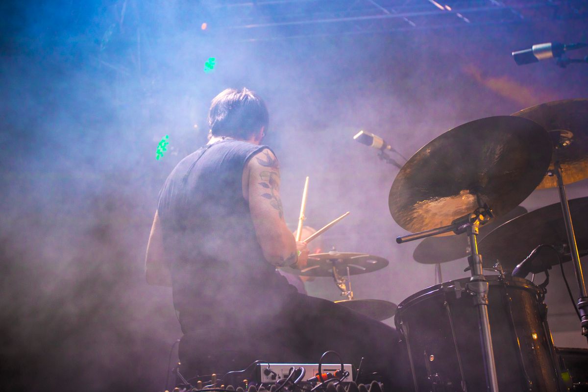 Drummer behind the kit, backlit through blue stage smoke