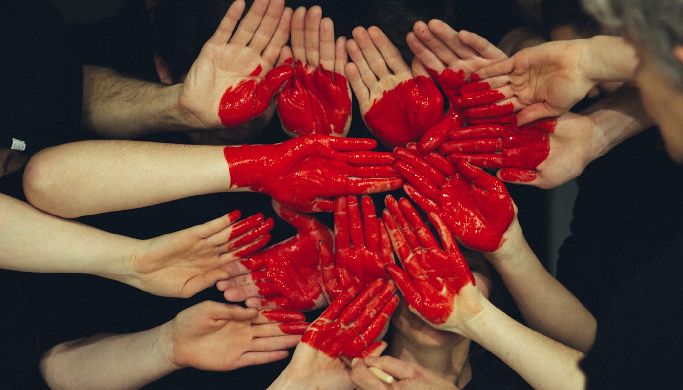Many open hands joined together painted to form a single red heart