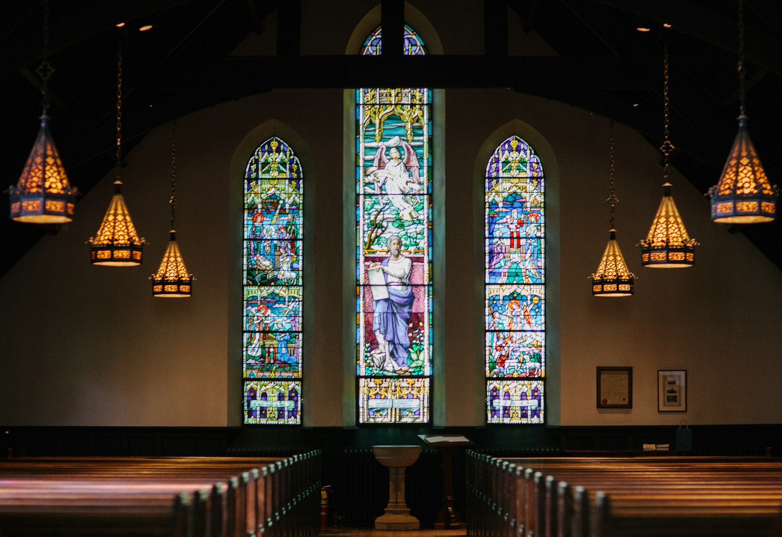 Sunlit church sanctuary with tall stained-glass windows and wooden pews