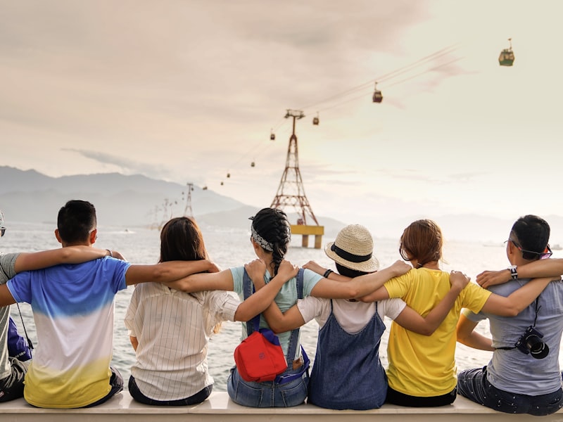 Group of teenagers sitting together by the water, arms around each other