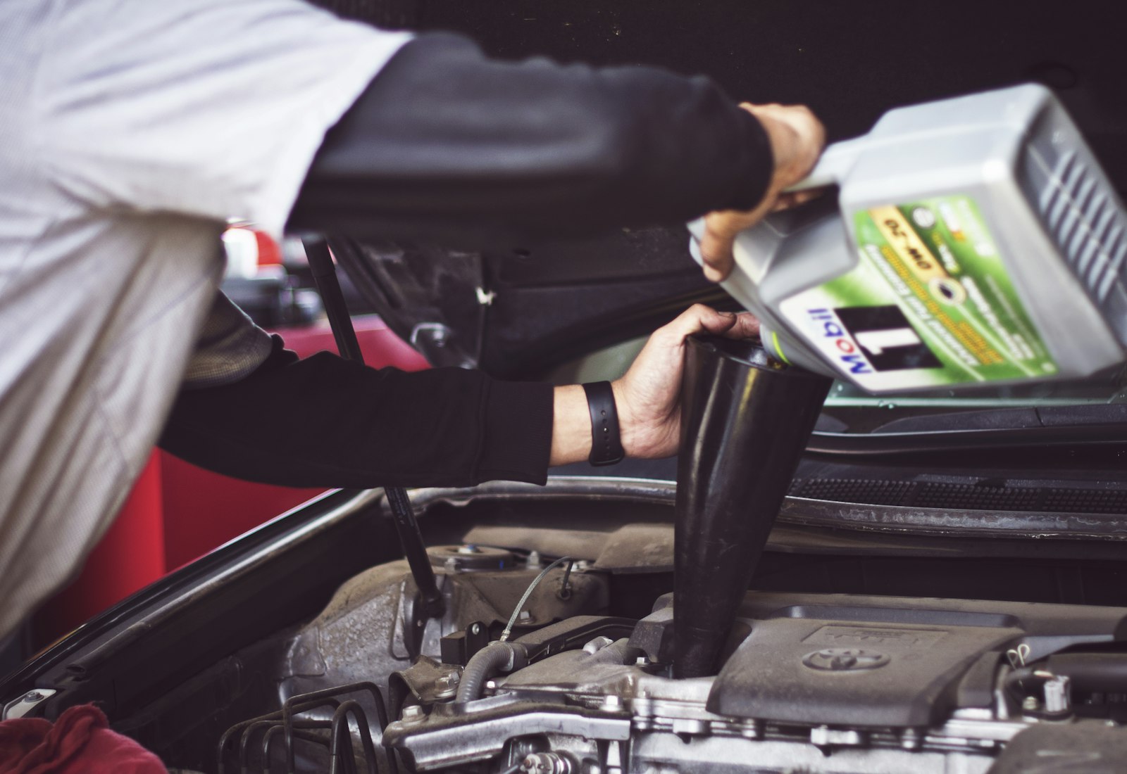 Mechanic topping up engine oil under the hood of a car at Apex Auto Works