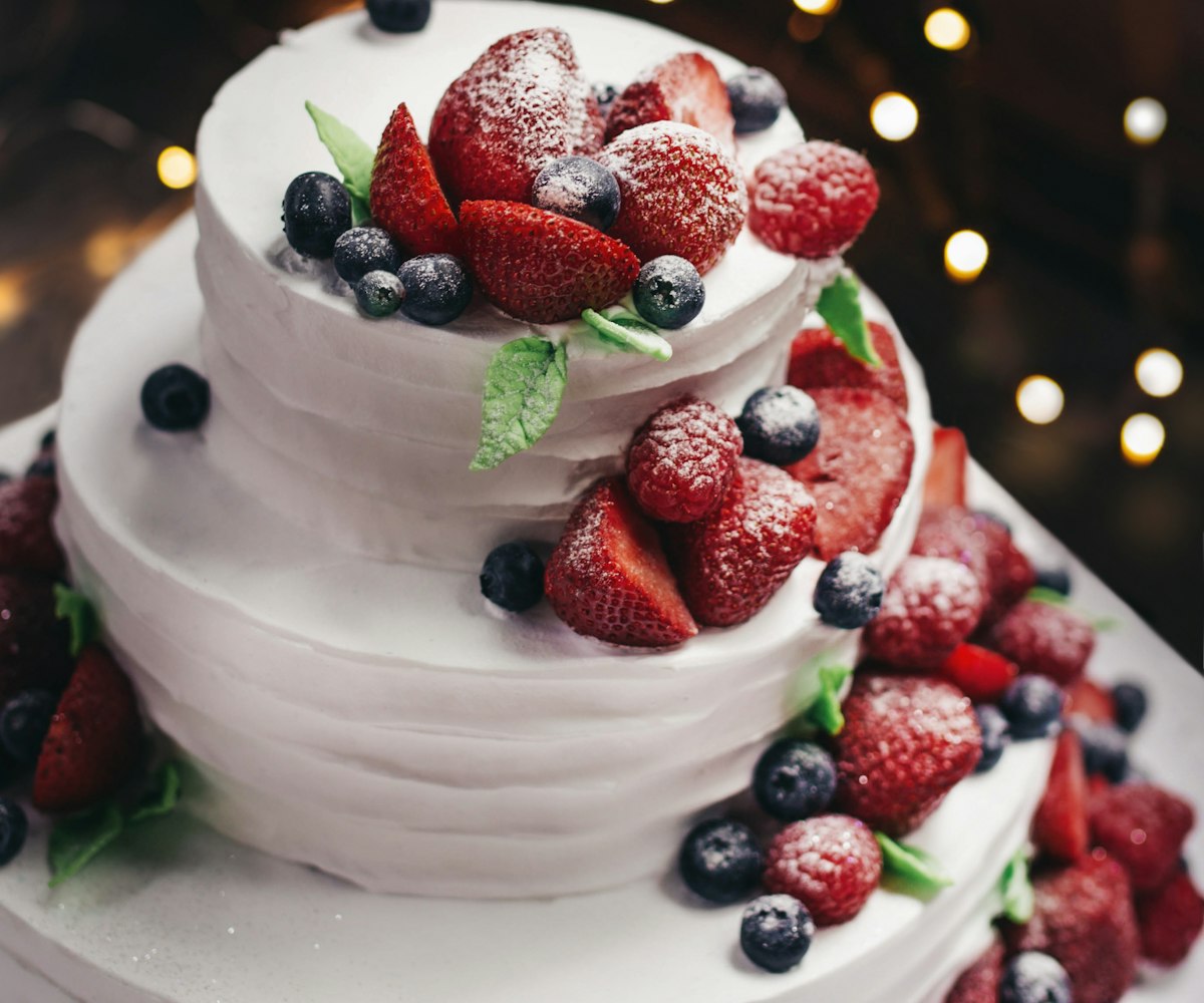 Two-tier white celebration cake topped with fresh berries and dusted with sugar