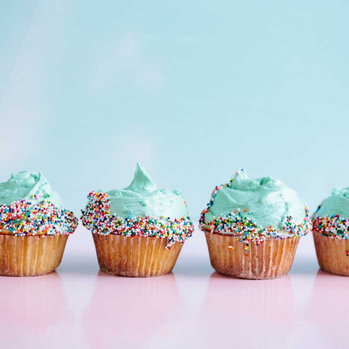 A row of vanilla cupcakes topped with mint-green frosting and rainbow sprinkles