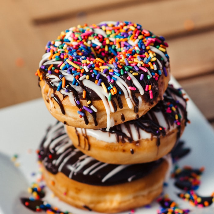 Stack of glazed donuts decorated with chocolate drizzle and rainbow sprinkles