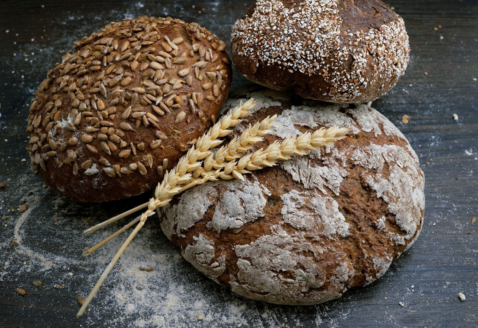 Three rustic artisan loaves dusted with flour on a wooden board with wheat stalks