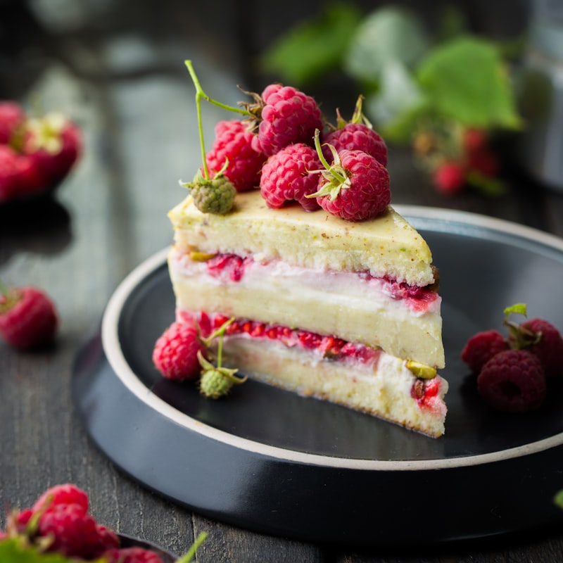 A slice of raspberry and pistachio layer cake topped with fresh raspberries.