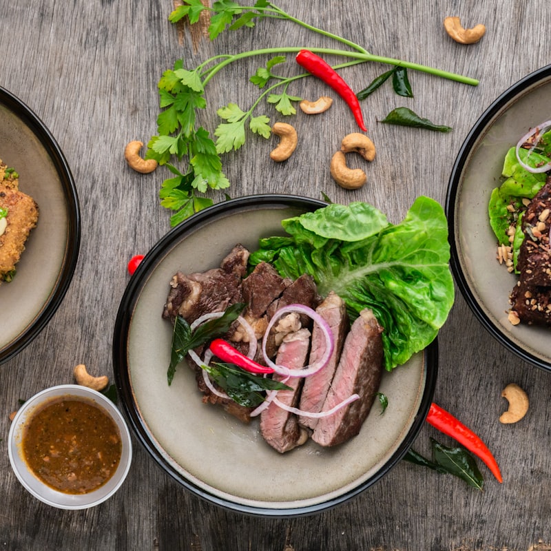 Plates of sliced beef, fresh herbs, and salad photographed from above on rustic wood.