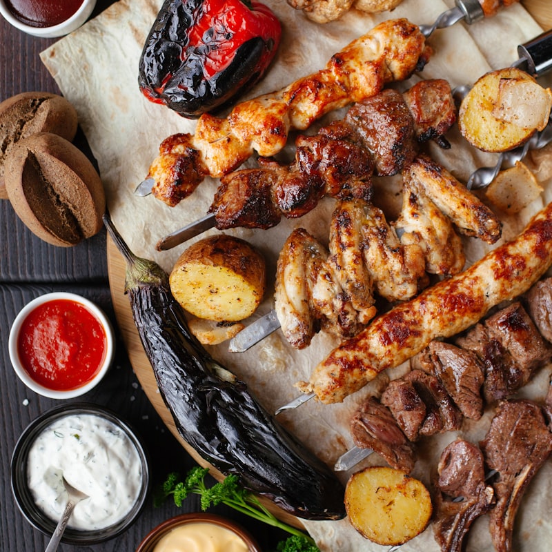 A grazing platter of grilled meat skewers, roast potatoes, peppers, and dipping sauces.