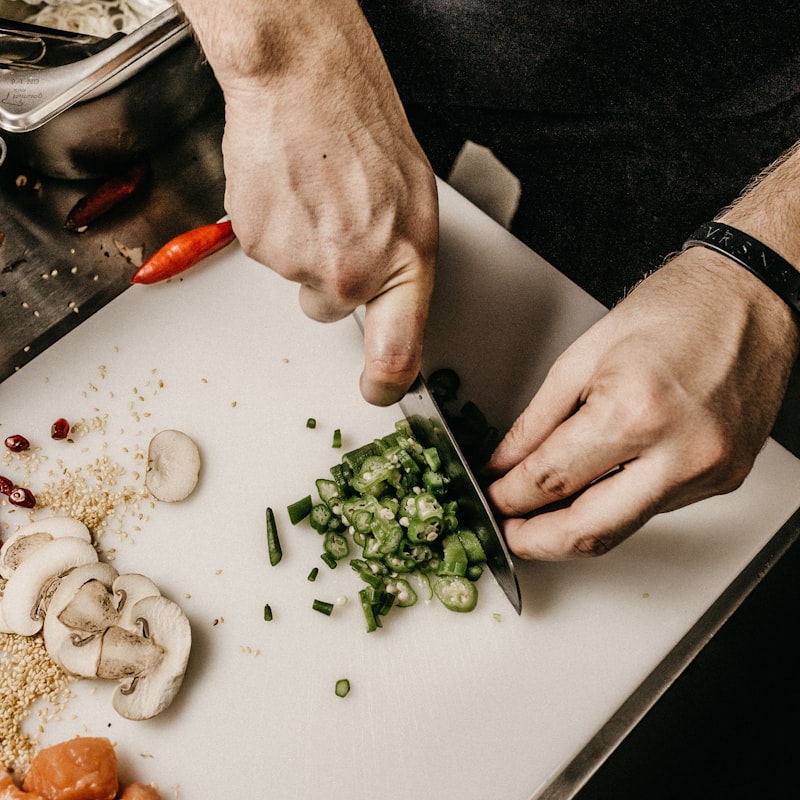 A chef's hands finely chopping fresh chilies and herbs on a board in the kitchen.