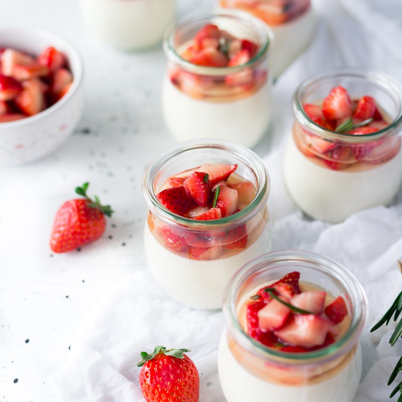 Individual panna cotta dessert jars topped with macerated strawberries and mint.