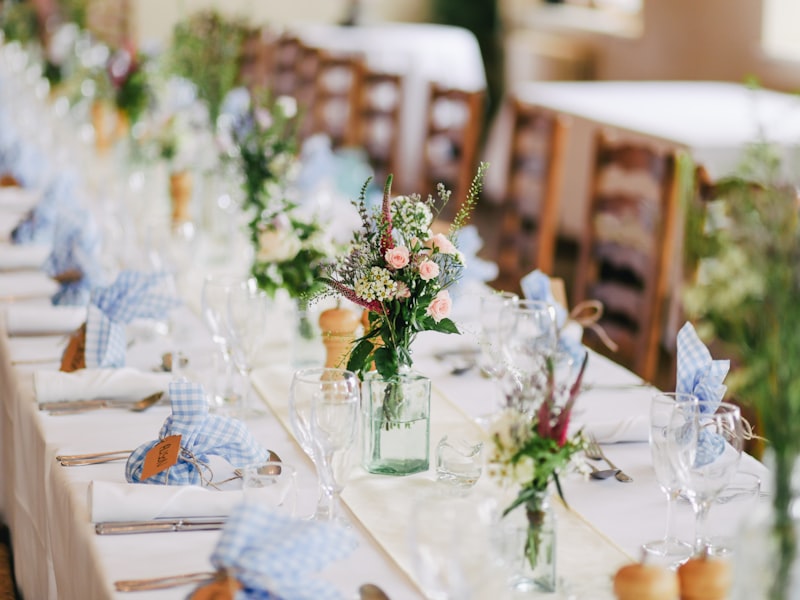 A long wedding banquet table set with linen, wildflower posies, and polished glassware.
