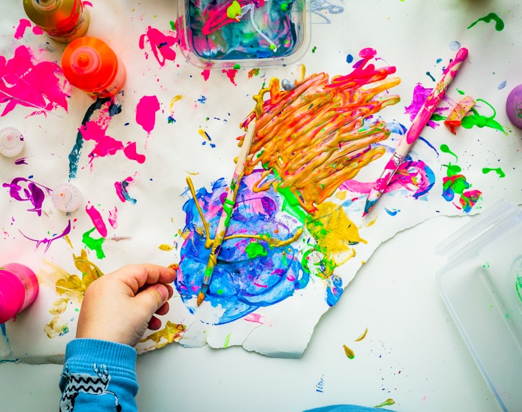 A child's colorful finger-painting in progress on a busy art table