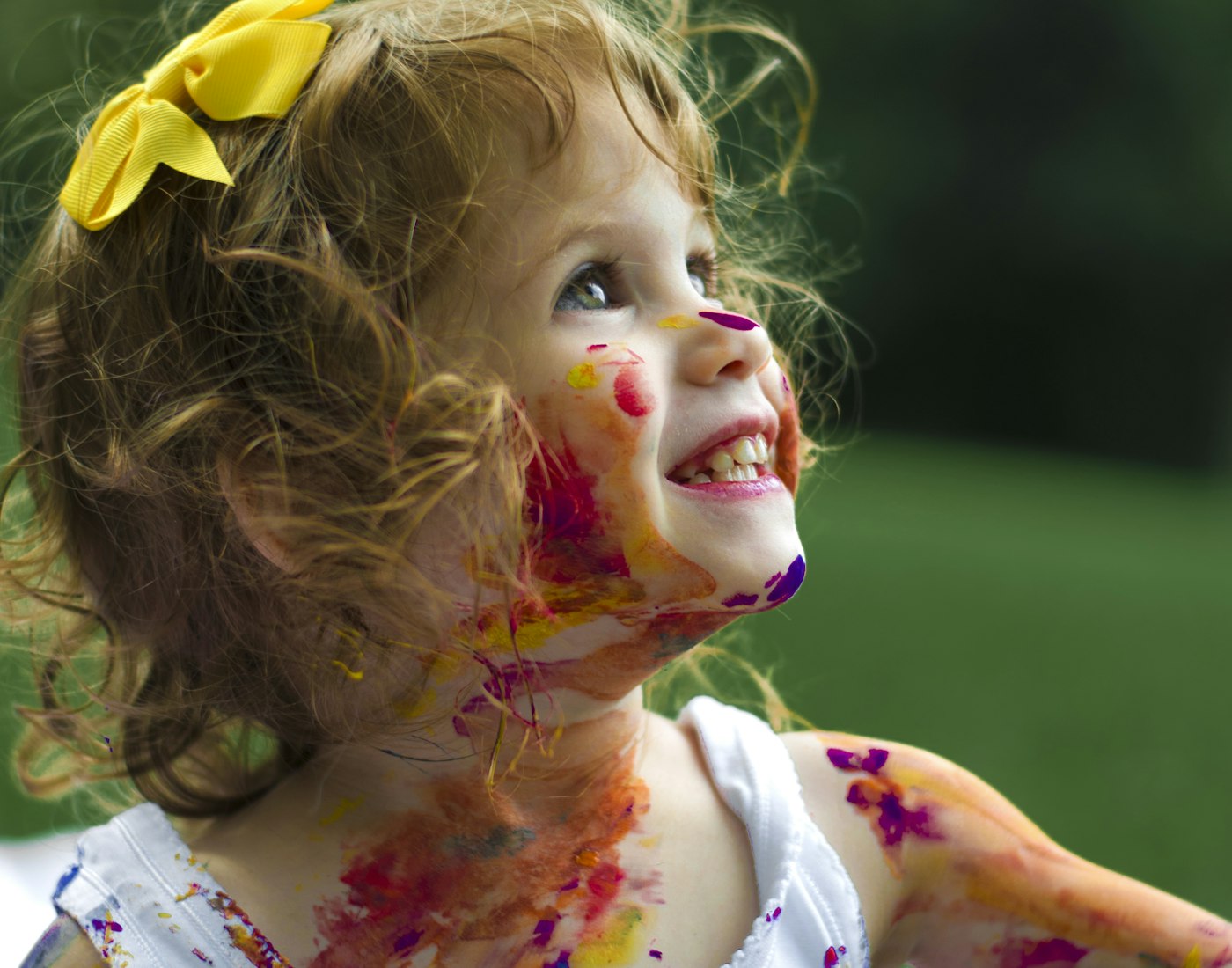 A joyful preschooler laughing outdoors, face brightly painted after an art day